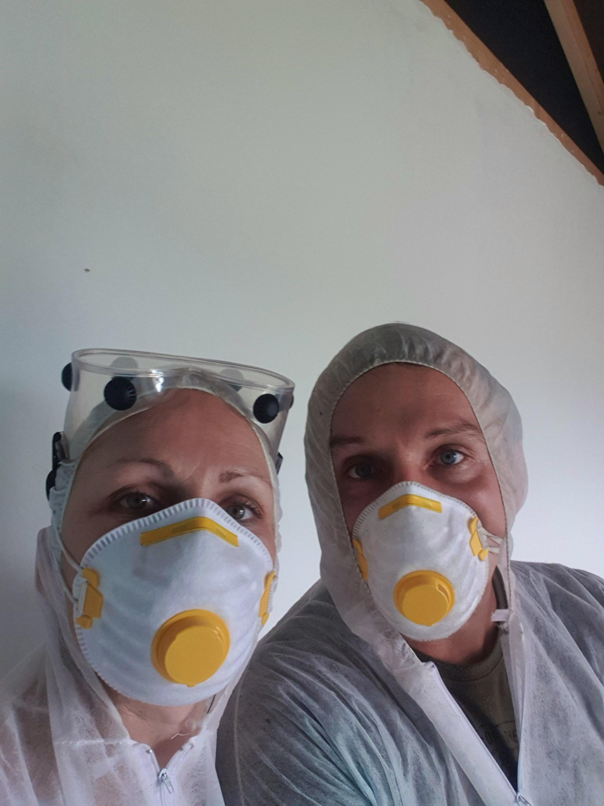 Baupaar in Schutzanzügen und Atemschutzmasken beim Schleifen der Innenwände