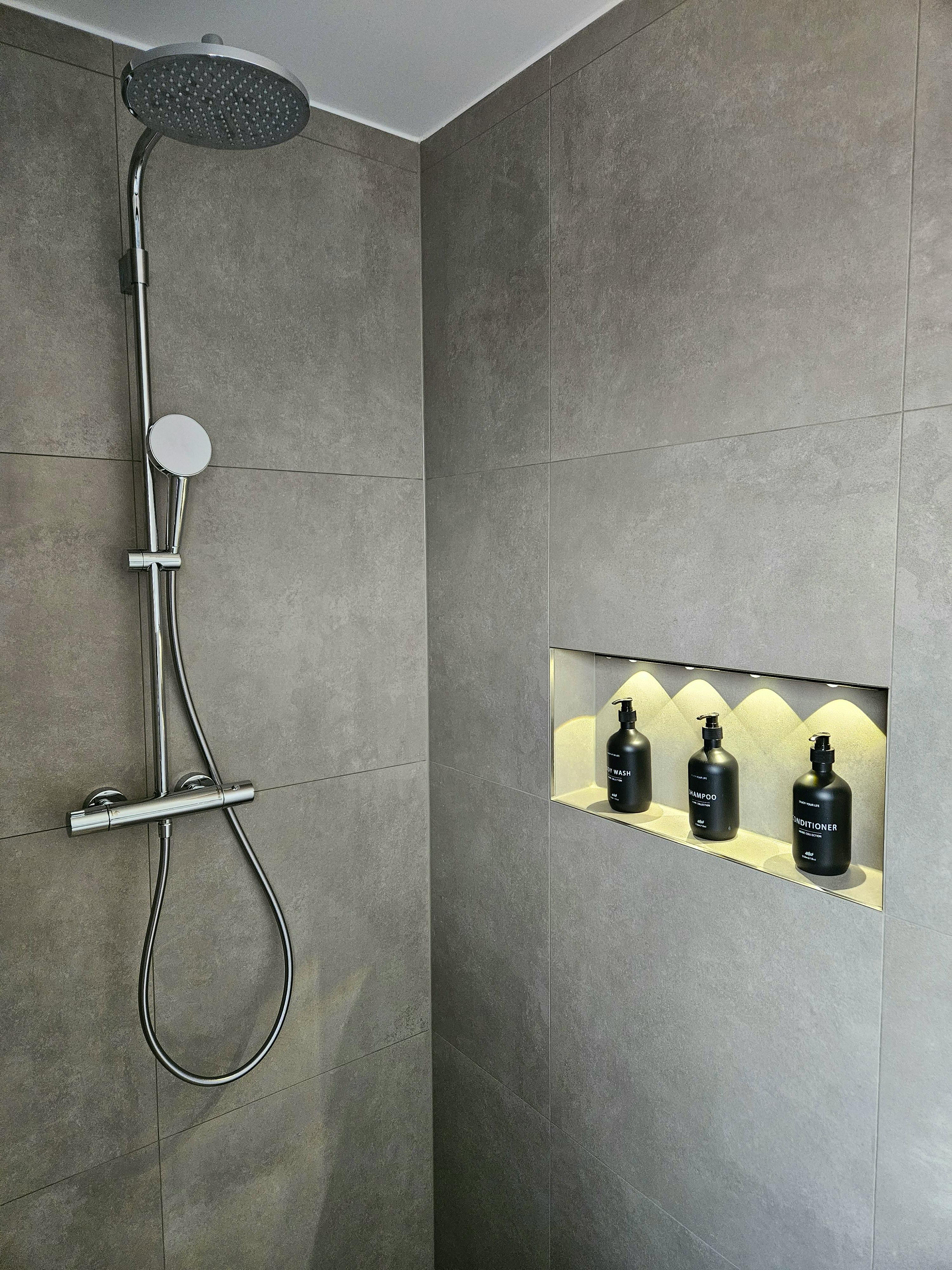 Badezimmer mit grauen Großformat-Fliesen, Regendusche und beleuchteter Wandnische im Kapitänshaus