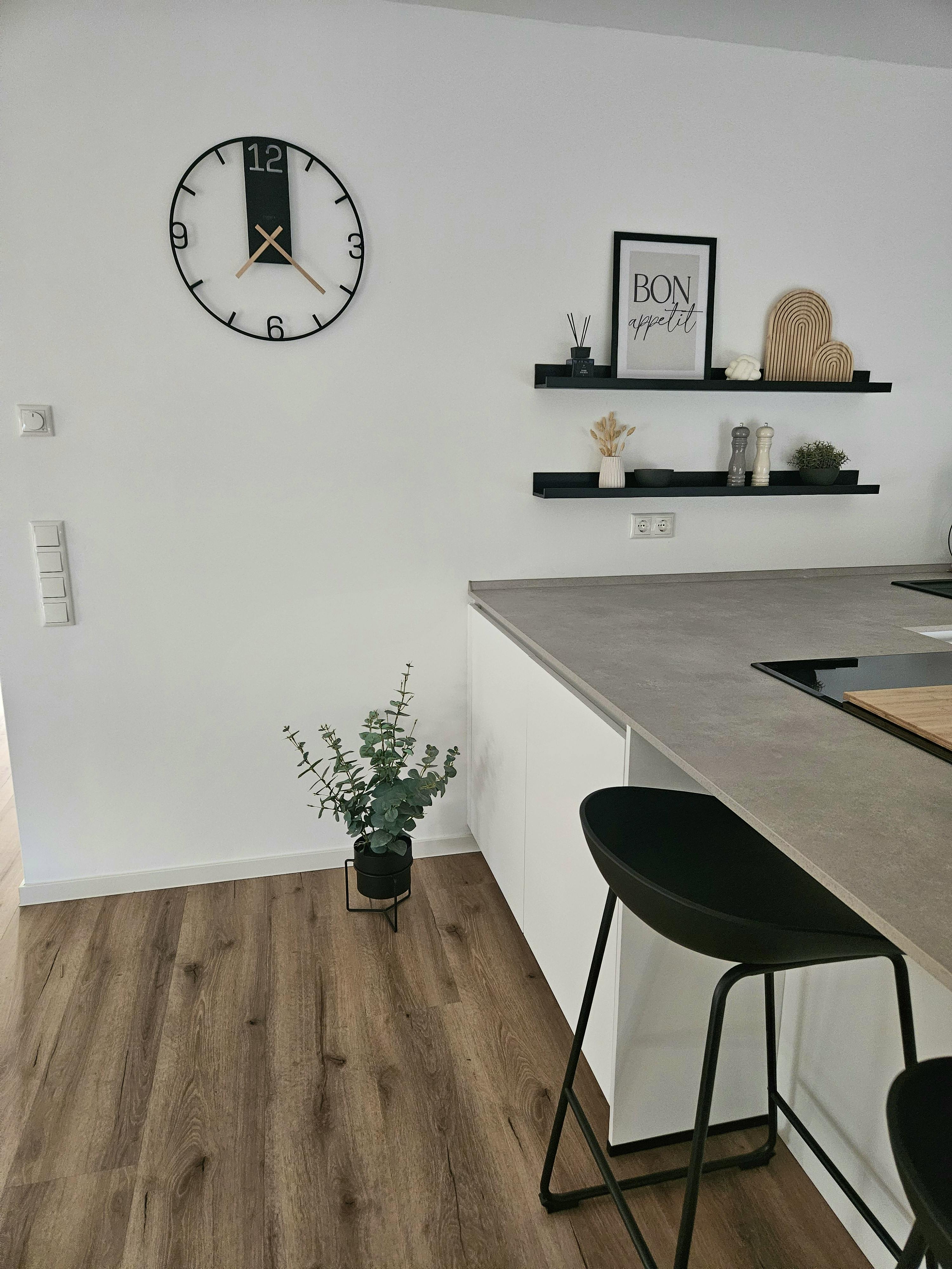 Offene Küche mit weißen Fronten, grauer Betonoptik-Arbeitsplatte, schwarzem Barhocker und Wandregalen im Kapitänshaus
