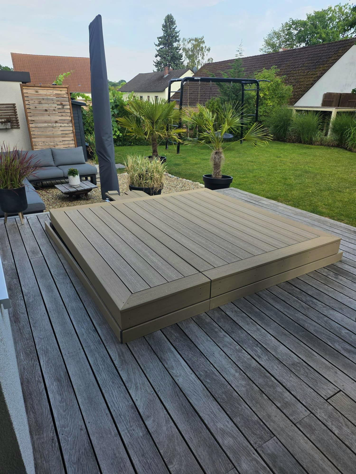 Fertig verlegte Kerama-Kunststoffdielen als Pool-Abdeckung, im Hintergrund Garten mit Palmen und Kinderspielgerüst