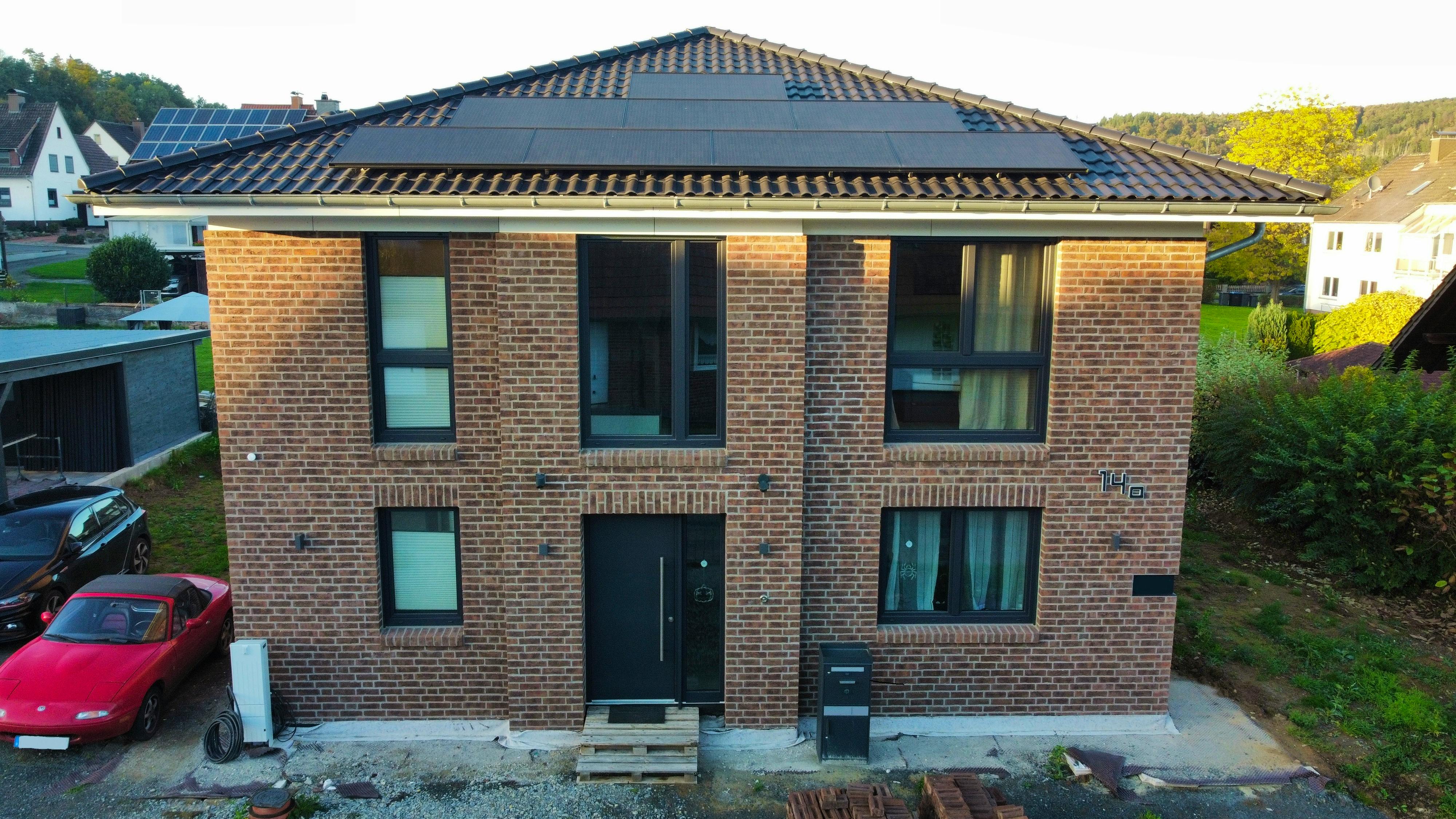 Frontalansicht der Viebrockhaus Maxime 710 II in Bodenfelde – Klinkerfassade, PV-Anlage auf dem Walmdach, dörfliche Nachbarschaft