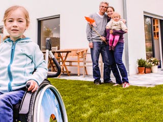 Mädchen im Rollstuhl mit ihren Eltern vor ihrem Haus