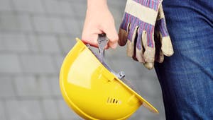 Gelber Bauhelm wird vom Bauherr in der Hand gehalten