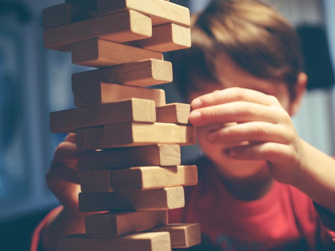 Junge baut Turm aus Holzbausteinen Jenga