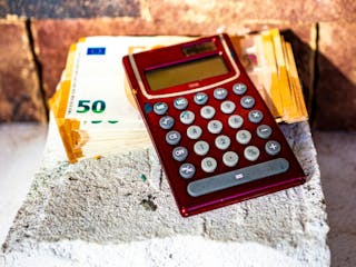 Berechnung Nebenkosten Hausbau - Taschenrechner mit Geldscheinen auf Mauersteinen