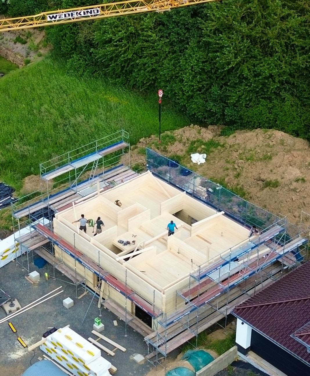 Luftbild des Blockhauses während der Bauphase, Doppelwandaufbau und Raumaufteilung des Obergeschosses von oben sichtbar, Baukran und Gerüst