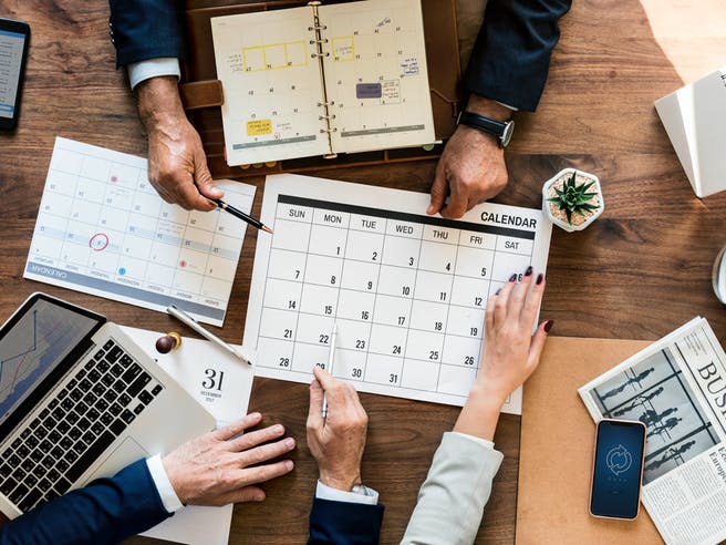 Drei Menschen planen Hausbau am Schreibtisch mit Kalender