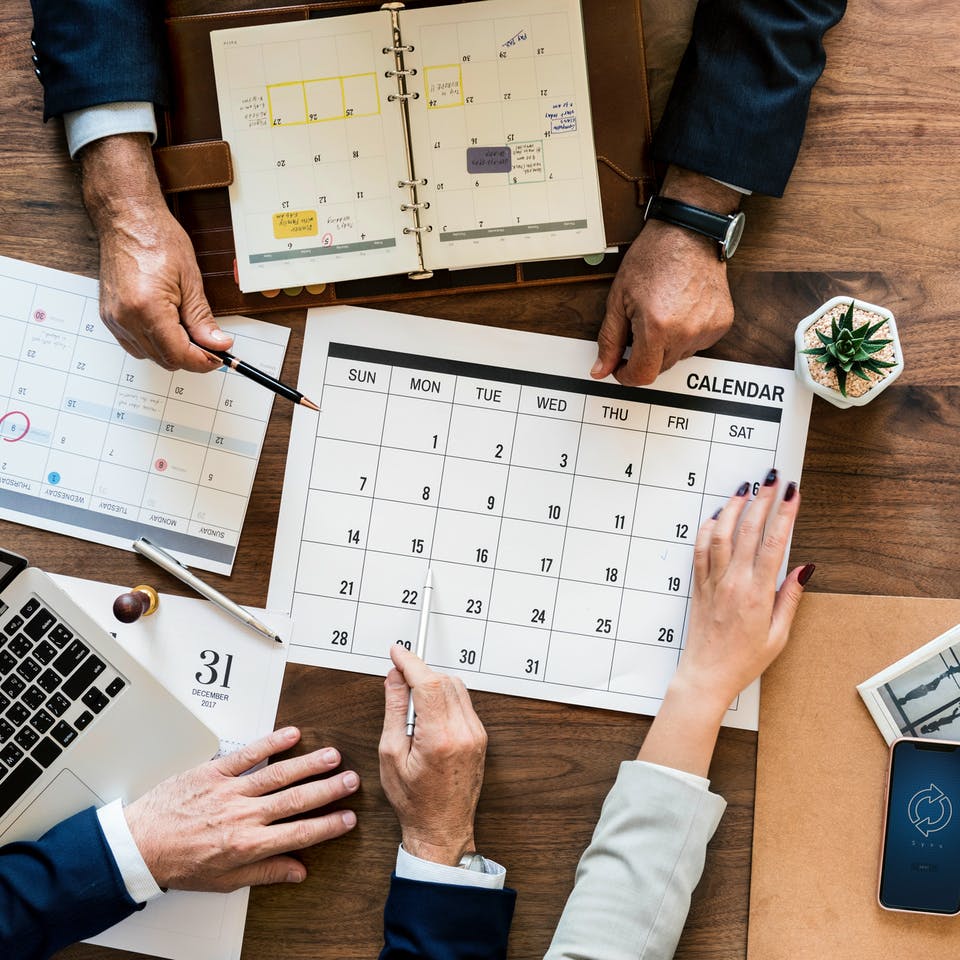 Drei Menschen planen Hausbau am Schreibtisch mit Kalender