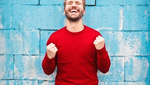 Mann in rotem Pullover steht vor einer blauen Wand und freut sich