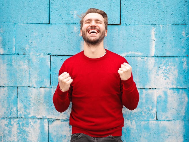 Mann in rotem Pullover steht vor einer blauen Wand und freut sich