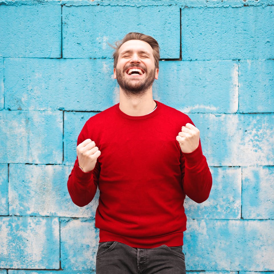 Mann in rotem Pullover steht vor einer blauen Wand und freut sich