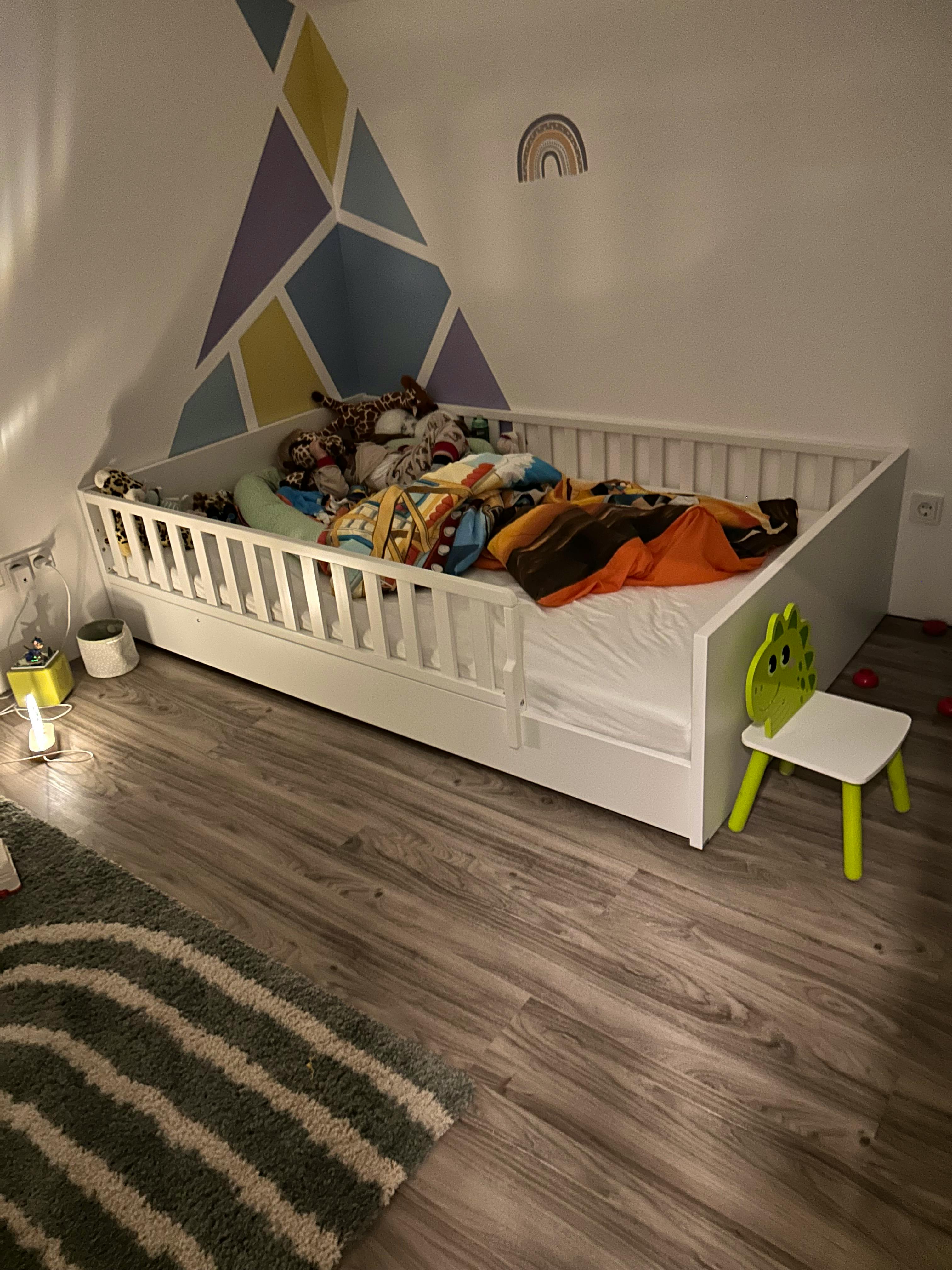 Kinderzimmer im Hanse-Haus-Fertighaus – geometrisches Bergmuster an der Wand in Blau, Gelb und Lila, Kinderbett mit Kuscheltieren, Vinylboden.