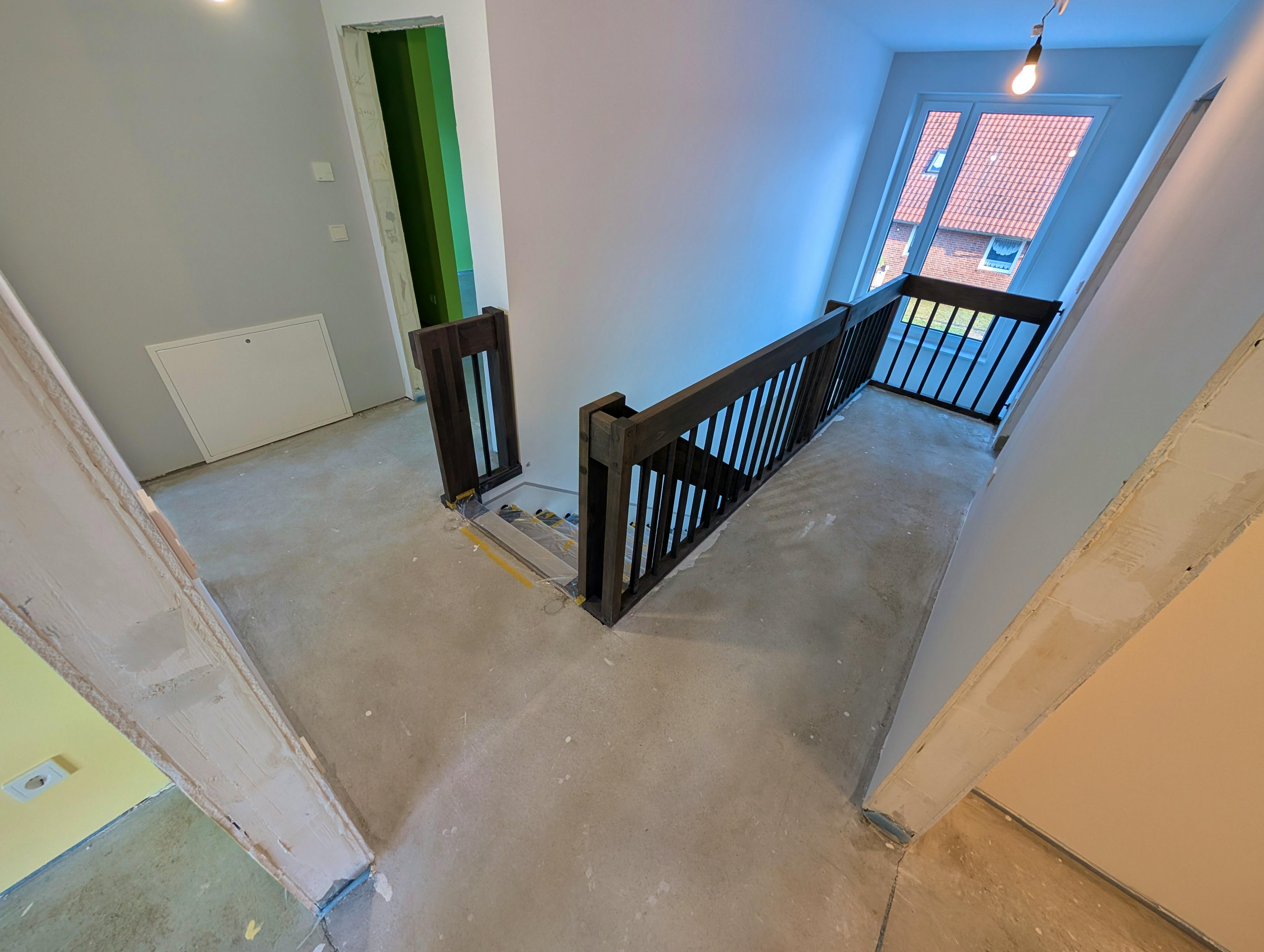 Galeriebereich im Obergeschoss während der Bauphase – Derstappen-Treppe aus schwarzer Buche bereits eingebaut, graue Q3-Wände und Rohbeton-Boden sichtbar