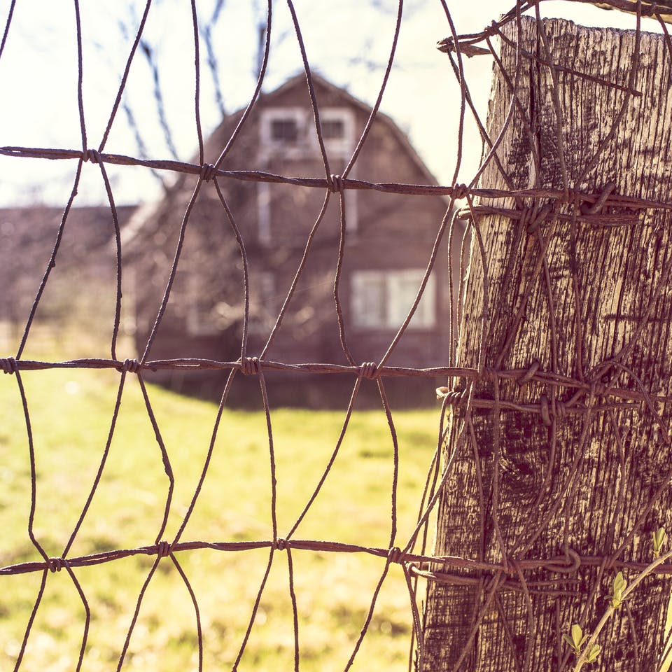 Ein Bauernhaus steht auf weitem Grundstück hinter einem Drahtzaun