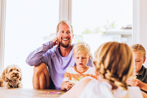 Vater sitzt mit seinen 3 Kindern am Tisch im Haus