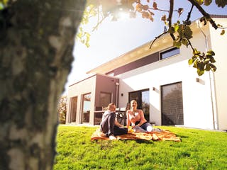 Familie sitzt im Garten vor neugebautem Haus