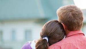 Bauherrenpaar blickt angelehnt aneinander auf ihr Haus