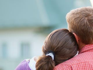 Bauherrenpaar blickt angelehnt aneinander auf ihr Haus