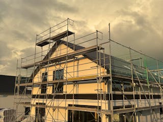 Haus im Rohbau mit Baugerüst und Schutznetz in der Abenddämmerung, Bauprojekt von Gina und Fabi