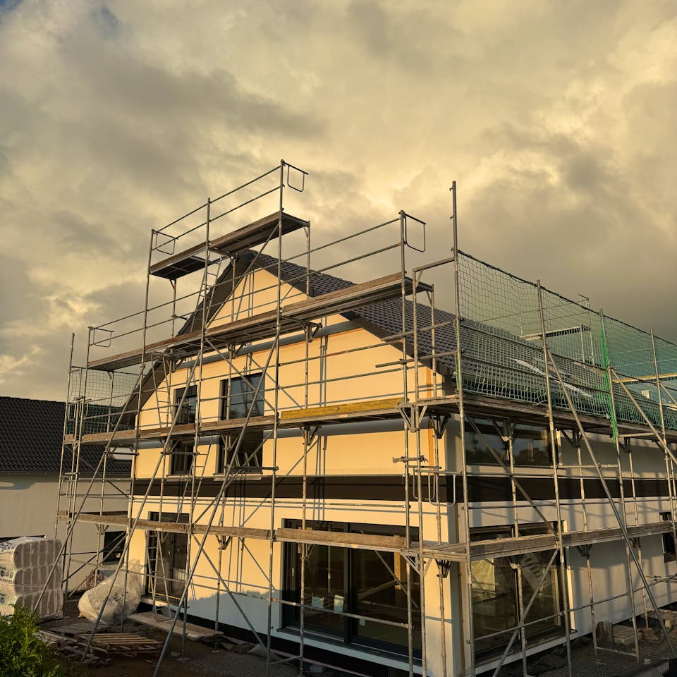 Haus im Rohbau mit Baugerüst und Schutznetz in der Abenddämmerung, Bauprojekt von Gina und Fabi