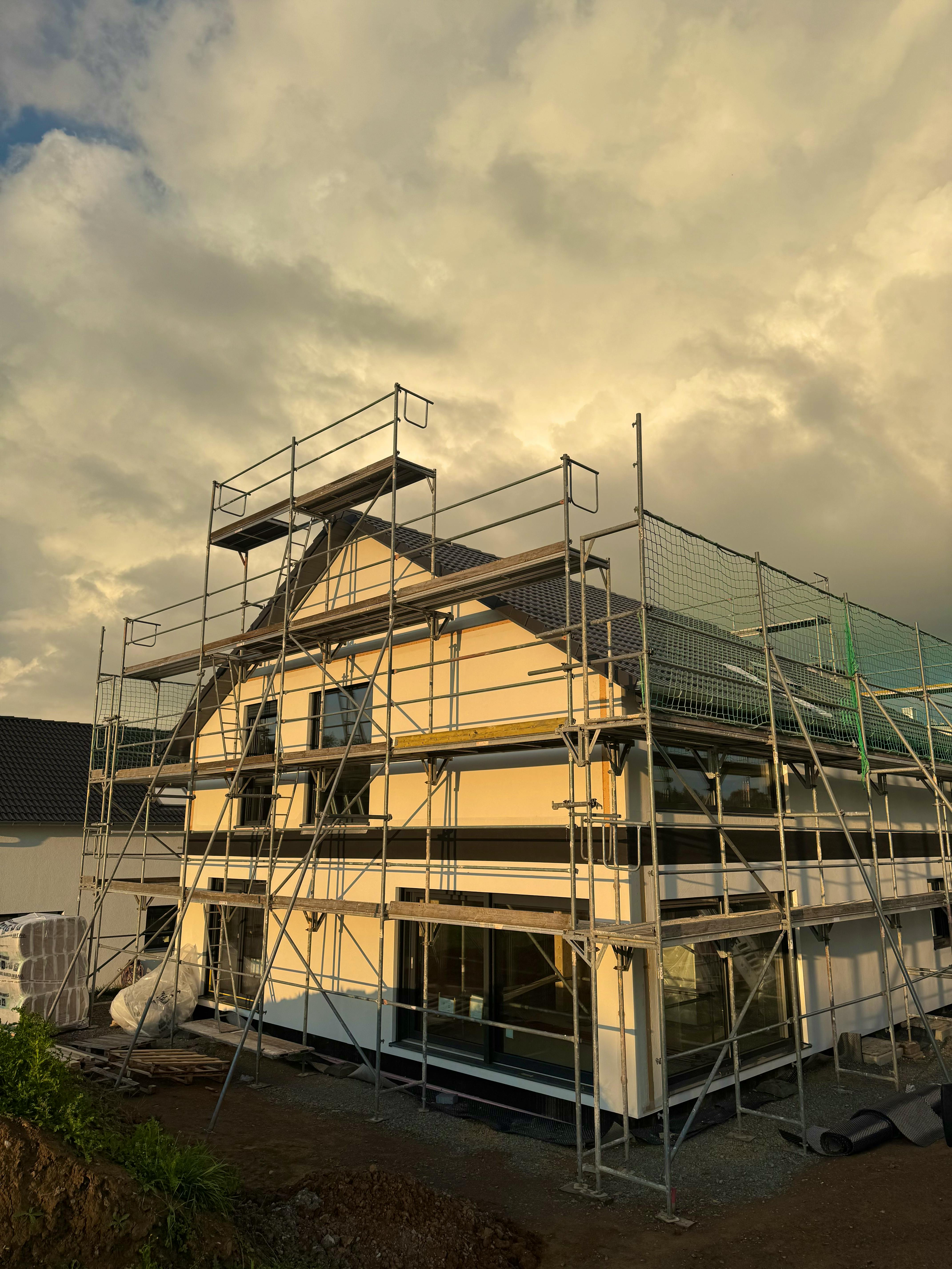 Haus im Rohbau mit Baugerüst und Schutznetz in der Abenddämmerung, Bauprojekt von Gina und Fabi