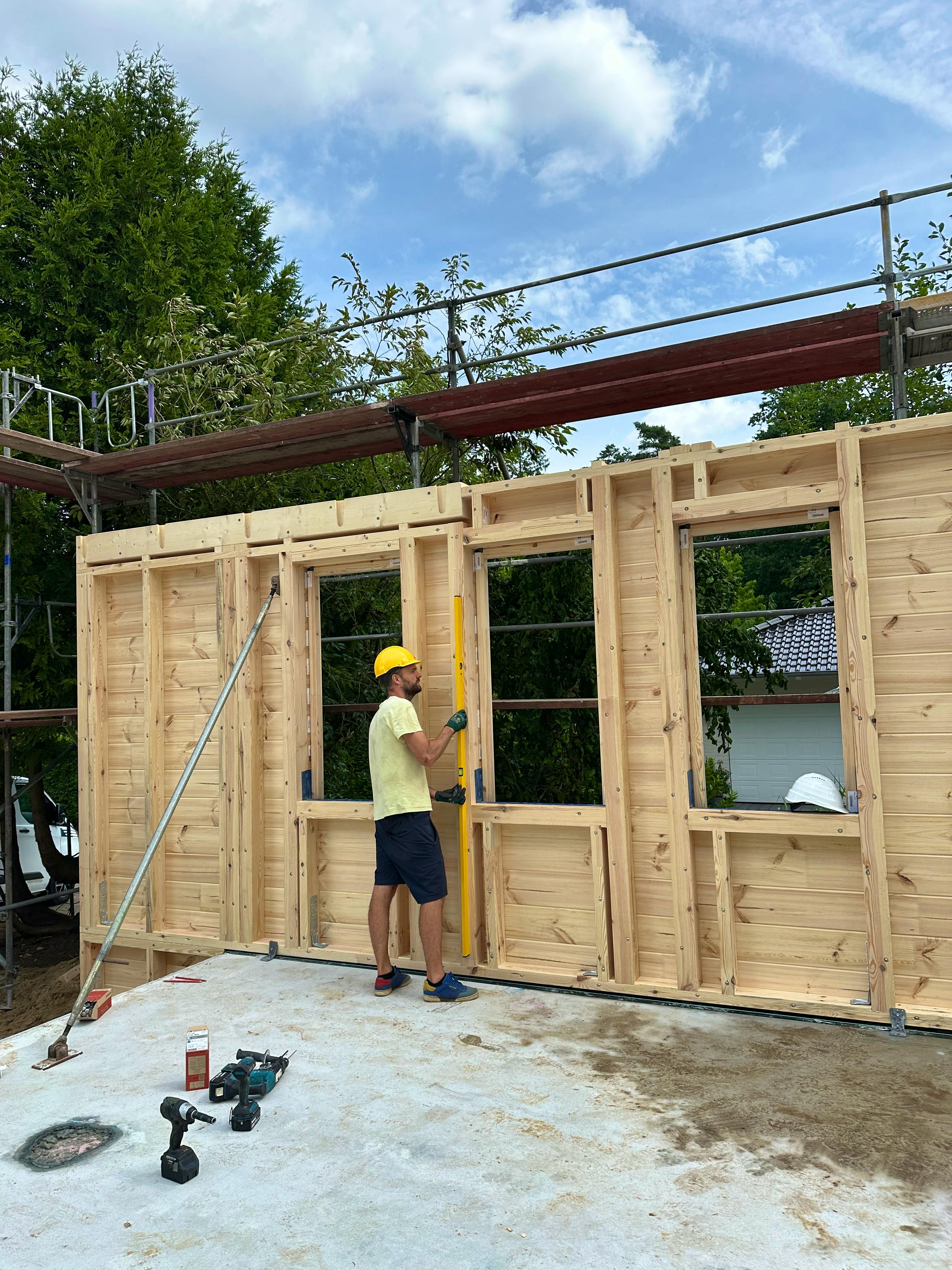 Lasse prüft mit Bauhelm und Wasserwaage die Ausrichtung einer vorgefertigten Fullwood-Blockwand auf der Baustelle