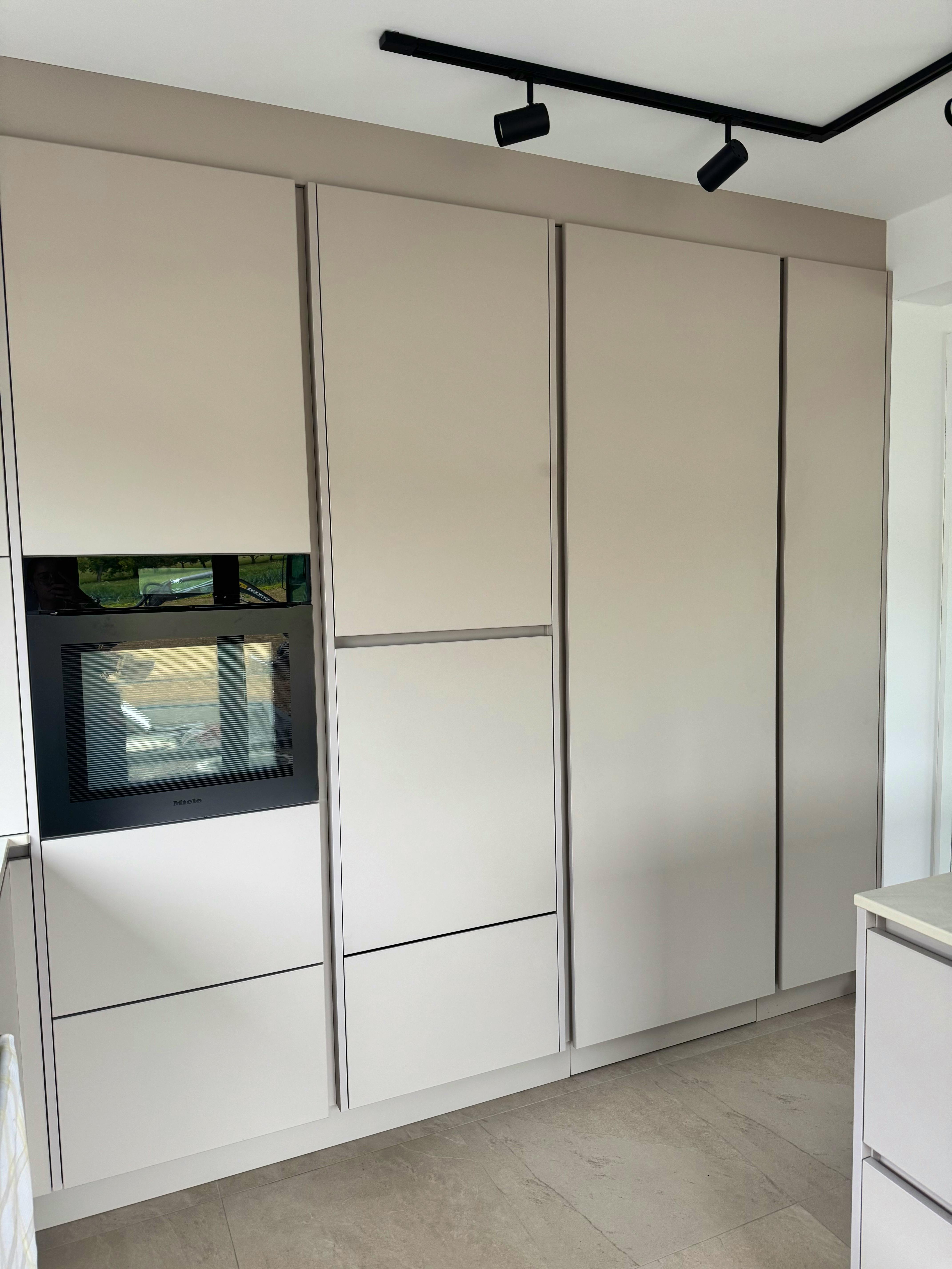 Geschlossene Küchenfront mit Miele-Backofen und beigefarbenen Schrankfronten