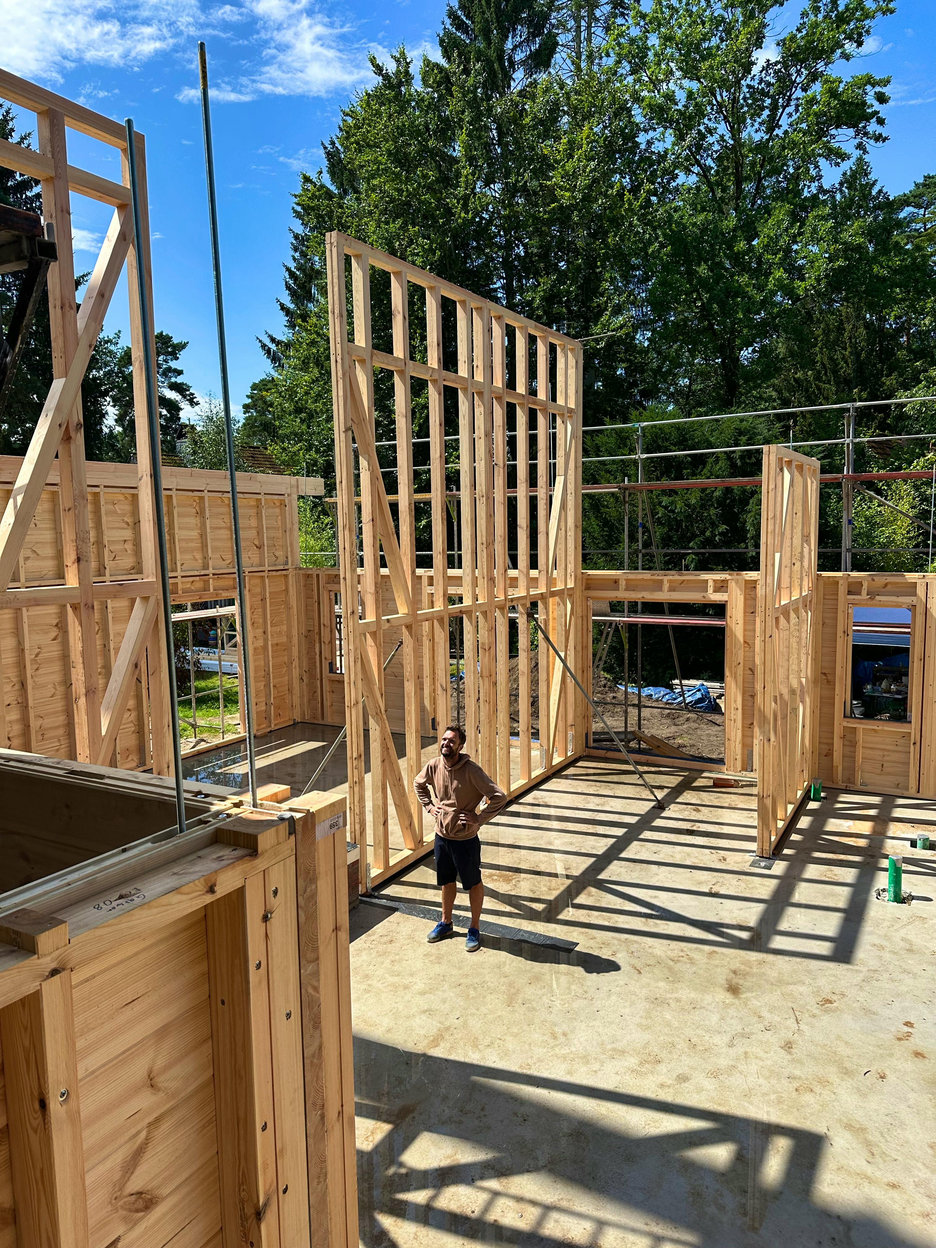 Lasse steht im Rohbau zwischen den Holzständerwerk-Innenwänden, im Hintergrund die massiven Blockbohlen-Außenwände