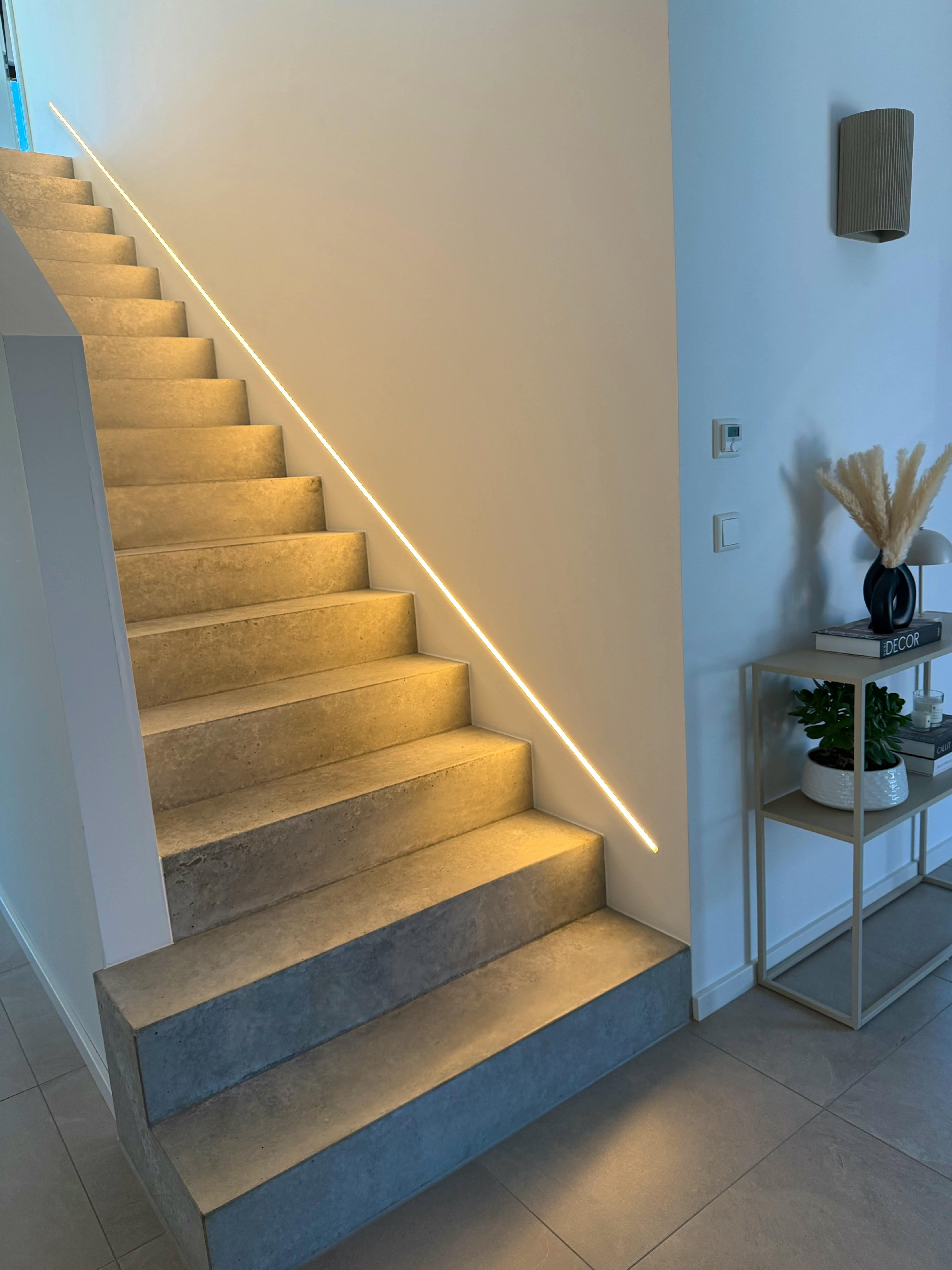 Sichtbetontreppe im Eingangsbereich mit warmem LED-Lichtband an der Wand