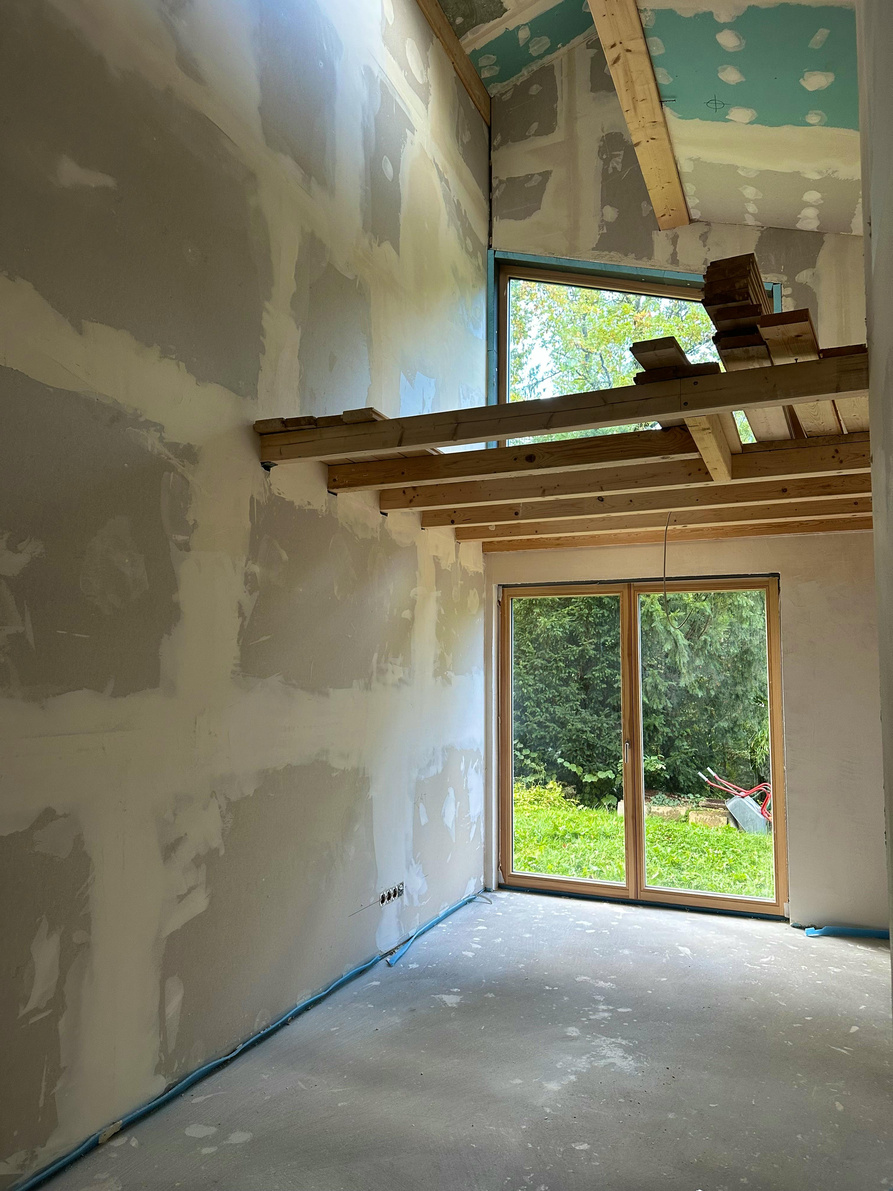 Raum im Fullwood-Blockhaus mit gespachtelten Rigips-Wänden, sichtbaren Holzbalken und bodentiefer Terrassentür zum Garten