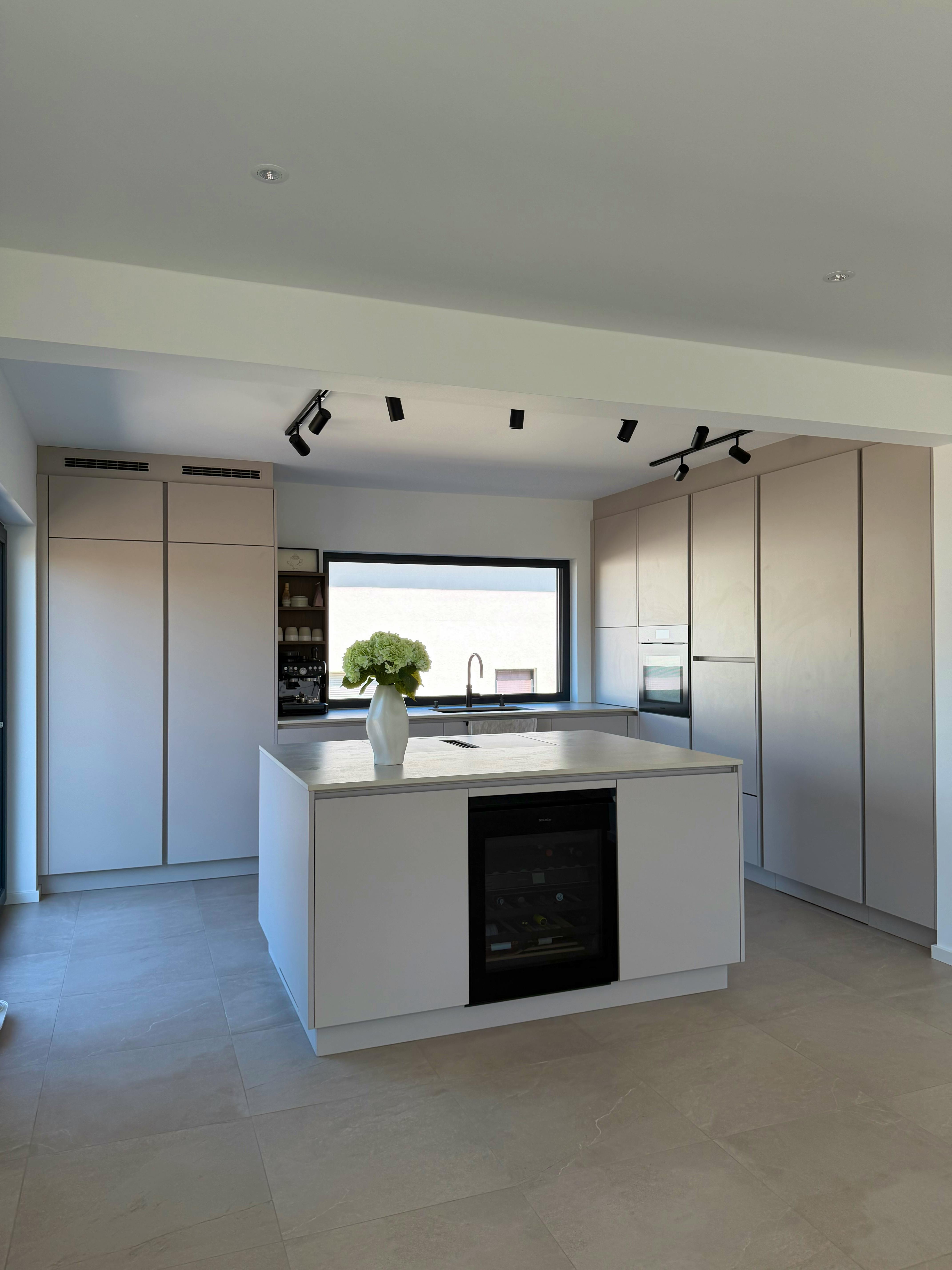 Moderne Küche mit hellen Beige-Fronten, schwarzem Weinkühlschrank in der Kochinsel und schwarzen Deckenspots