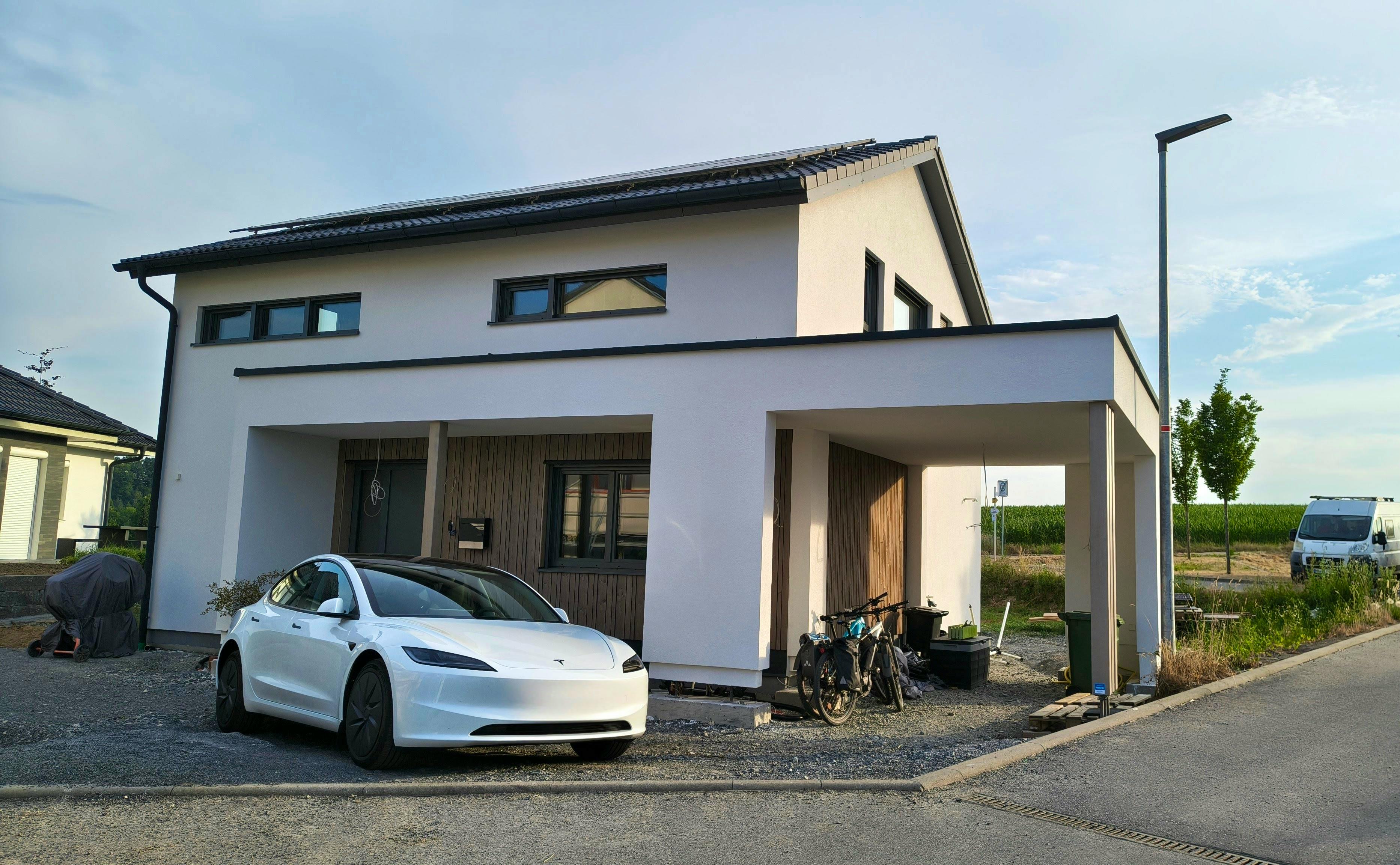 ELK Haus All-in-One 148 Frontansicht – weißer Putz mit Holzfassade am Eingang und Carport, Solaranlage auf dem Dach, Neubaugebiet in Hohenlohe