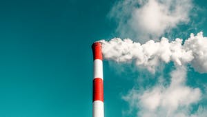Rot weißer Schornstein einer Fabrik ragt in blauen Himmel