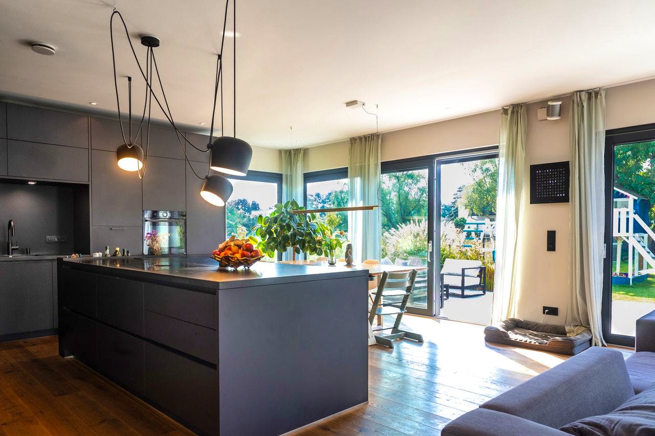 Offene Wohnküche mit dunkler Einbauküche, Kücheninsel und großer Glasfront im Kampa-Fertighaus