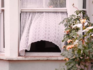 Offenes Fenster aus dem eine weiße Gardine rausweht