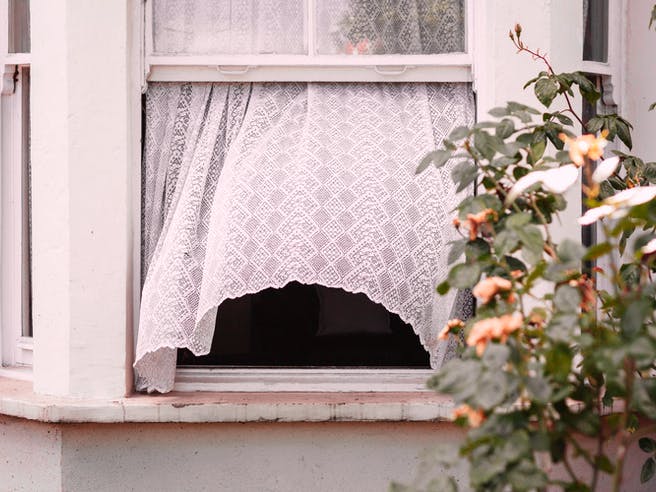 Offenes Fenster aus dem eine weiße Gardine rausweht