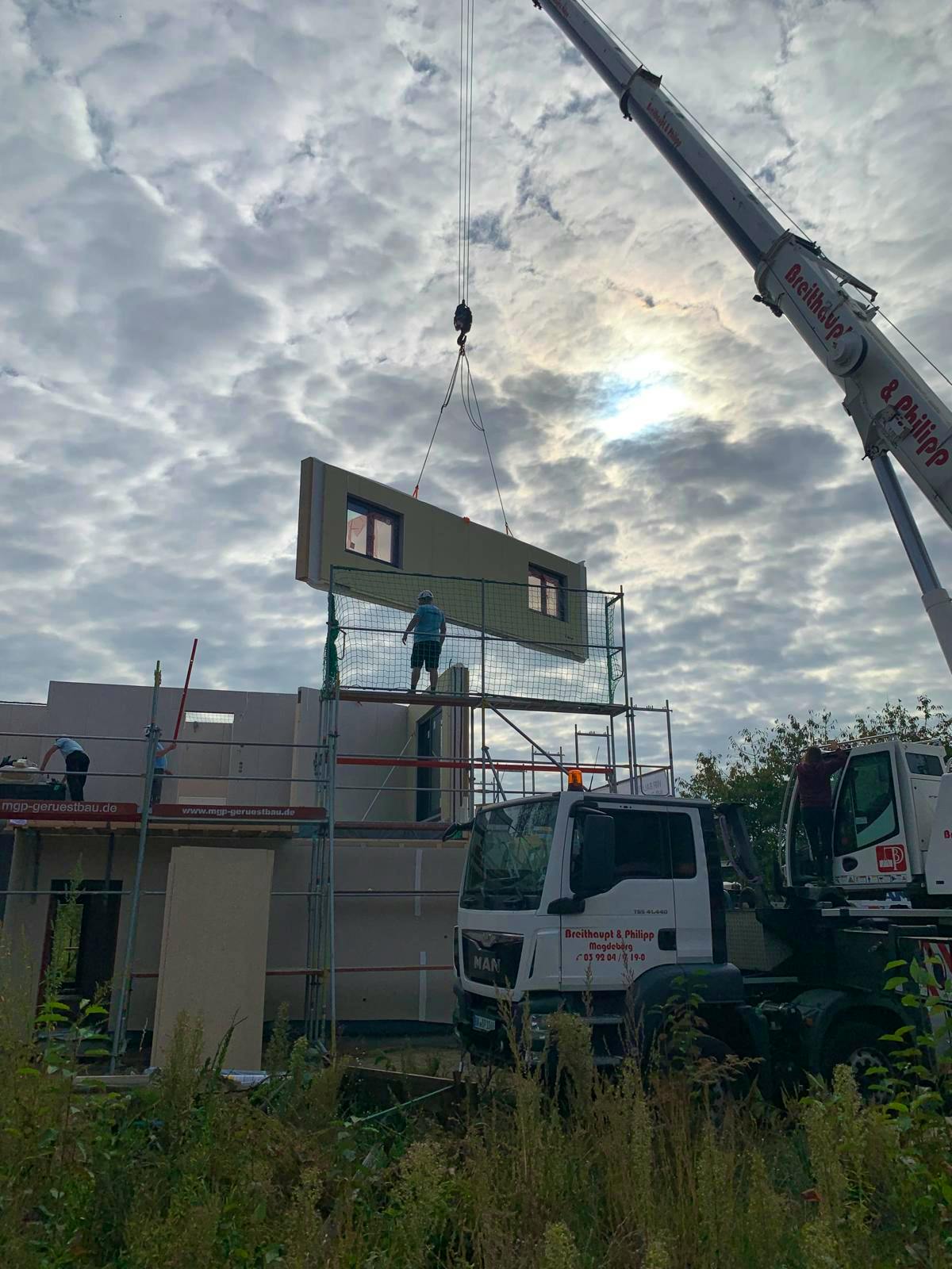 Mobilkran hebt vorgefertigtes Obergeschoss-Wandelement im Abendlicht auf den Rohbau in Berlin