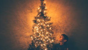 Junge sitzt unter einem Weihnachtsbaum mit Lichterkette