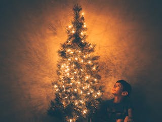 Junge sitzt unter einem Weihnachtsbaum mit Lichterkette