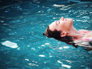 Frau schwebt im Pool mit geschlossenen Augen
