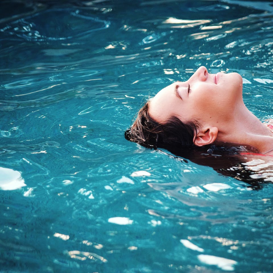 Frau schwebt im Pool mit geschlossenen Augen