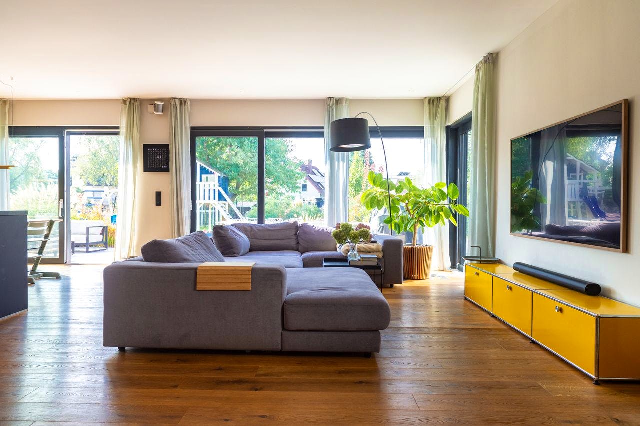 Wohnzimmer mit großer grauer Eckcouch, Fensterfront und Holzboden in der Kampa-Stadtvilla