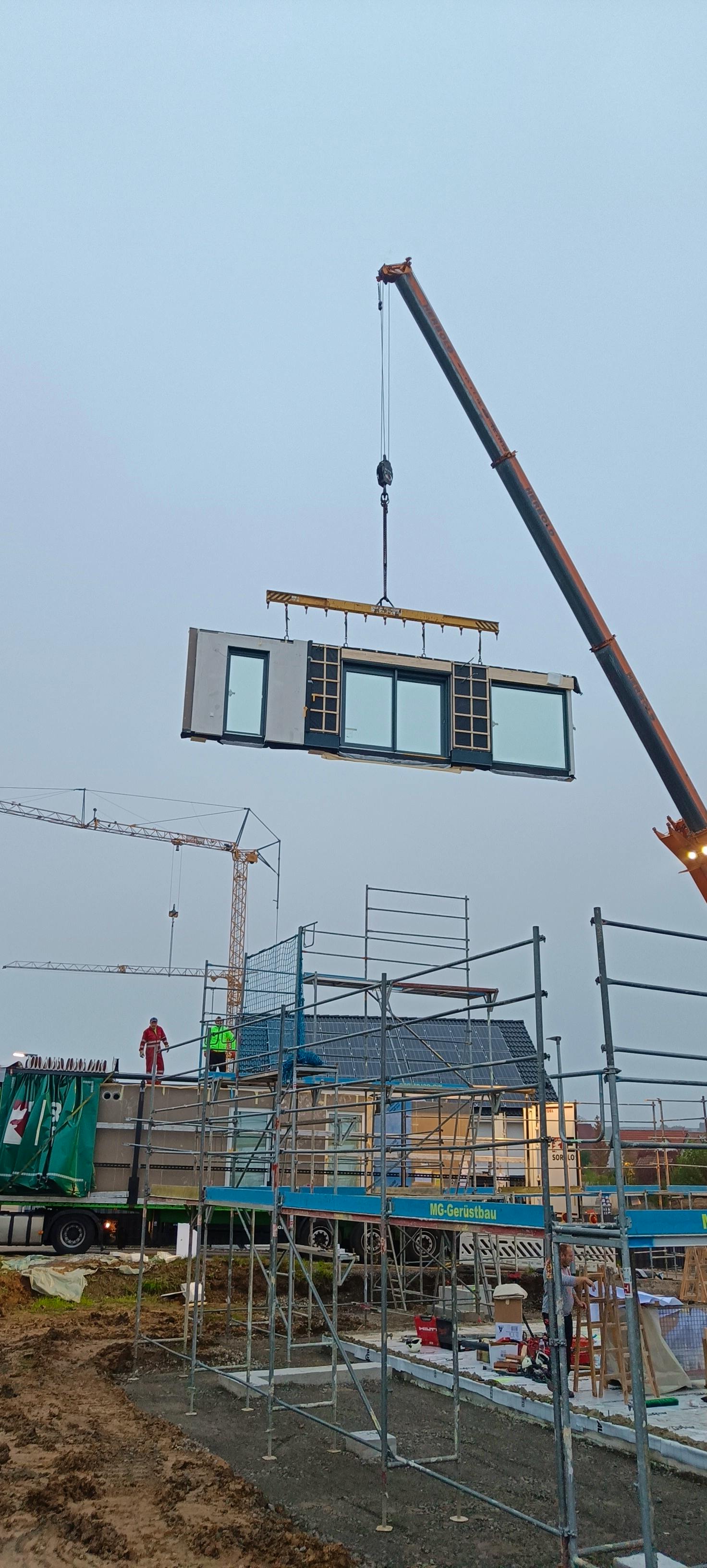 Stelltag des ELK Hauses in Hohenlohe – ein Kran hebt ein vorgefertigtes Wandelement mit Fenstern auf die Baustelle, nebliger Morgen