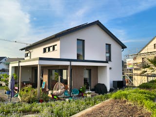 ELK Haus All-in-One 148 in Hohenlohe – Gartenansicht mit weißem Putz, Holzfassade unter der Terrassenüberdachung und Satteldach mit Solaranlage