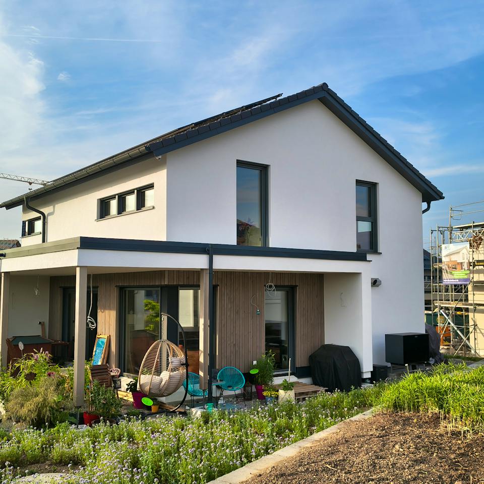ELK Haus All-in-One 148 in Hohenlohe – Gartenansicht mit weißem Putz, Holzfassade unter der Terrassenüberdachung und Satteldach mit Solaranlage