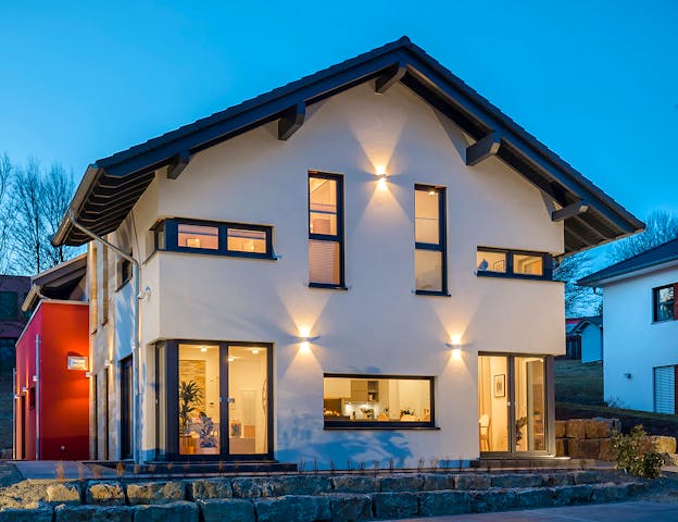 Bei diesem Fertighaus von OKAL Haus wurde der rote Anbau visuell abgesetzt und dient sowohl als Einliegerwohnung als auch als Balkon für das Haupthaus.
