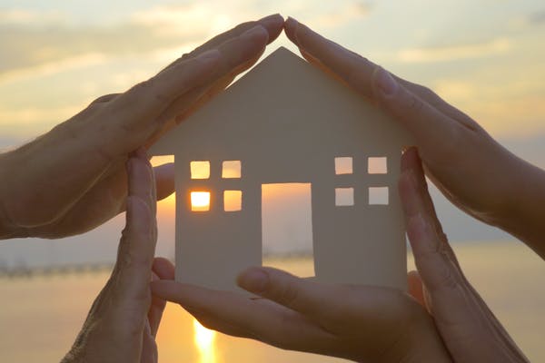 Mehrere Hände halten die Schablone eines Haus vor einen Sonnenuntergang